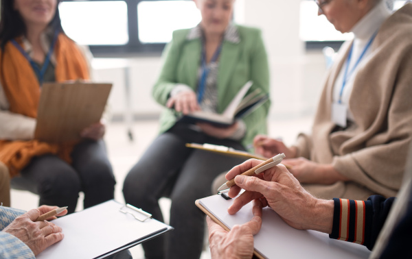 Excited elderly people attending a group therapy session at nursing house, positive senior man and woman sitting in circle, having conversation with psychologist