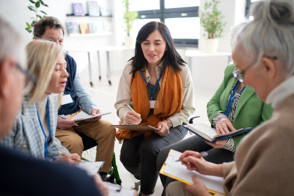 Excited elderly people attending a group therapy session at nursing house, positive senior man and woman sitting in circle, having conversation with psychologist