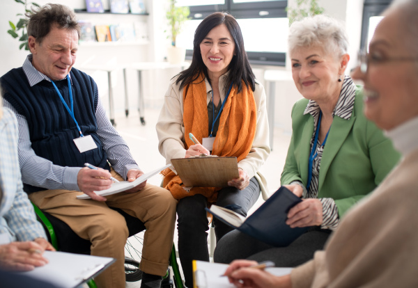 Excited elderly people attending a group therapy session at nursing house, positive senior man and woman sitting in circle, having conversation with psychologist