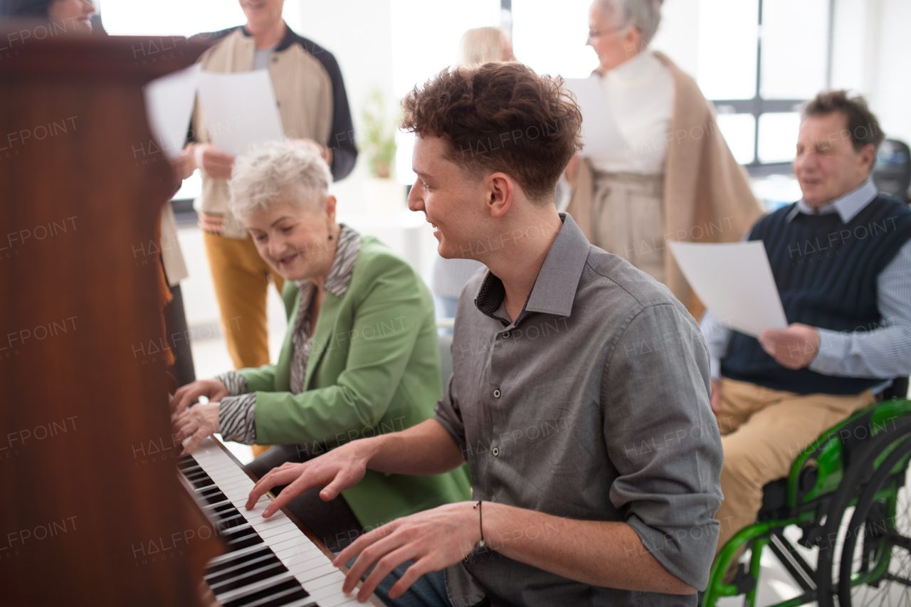 A senior woman with young teacher playing at piano in choir rehearsal.