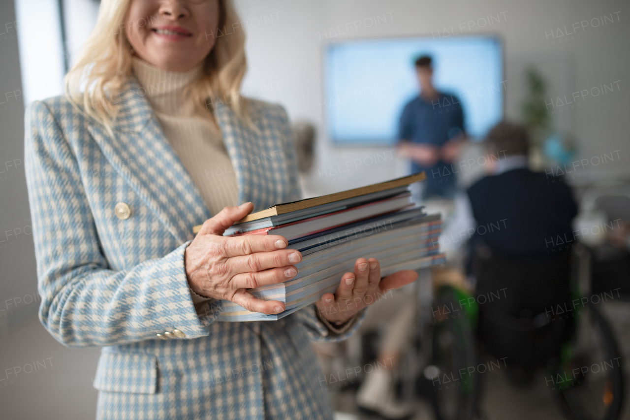 Happy senior woman student posing with a books in classroom.