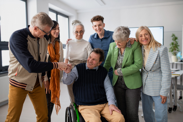 Happy senior students meeting with their friend on wheelchair at university. Social inclusion and university of third age concept.