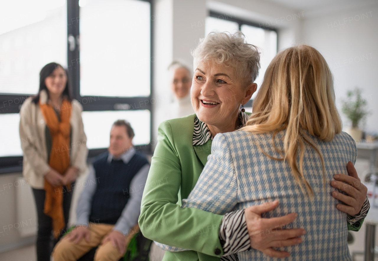 Happy senior women students meeting and hugging in a classroom.