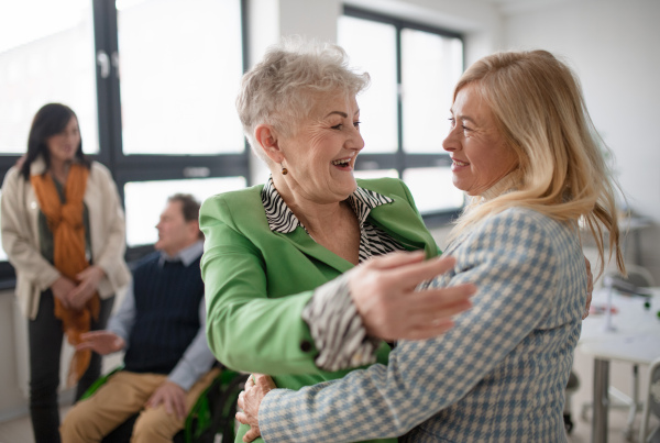 Happy senior women students meeting and hugging in a classroom.