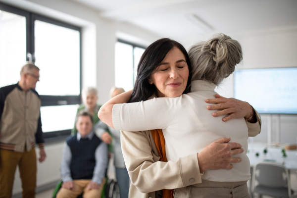 Happy senior women students meeting and hugging in a classroom.