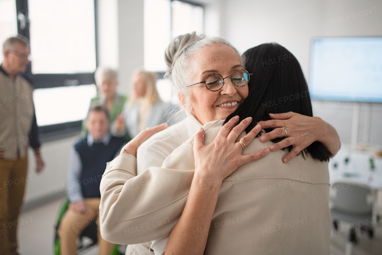 Happy senior women students meeting and hugging in a classroom.