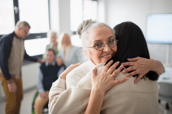 Happy senior women students meeting and hugging in a classroom.