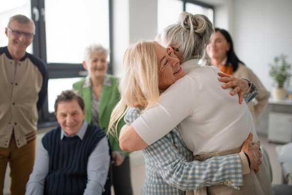 Happy senior women students meeting and hugging in a classroom.