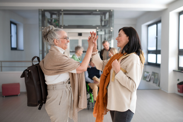 Happy senior women students meeting high fiving in a corridor at university.