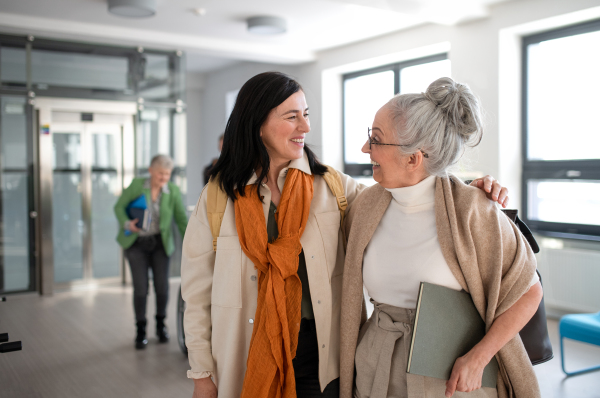 A happy mature woman student with book discussing with teacher in corridor in university.