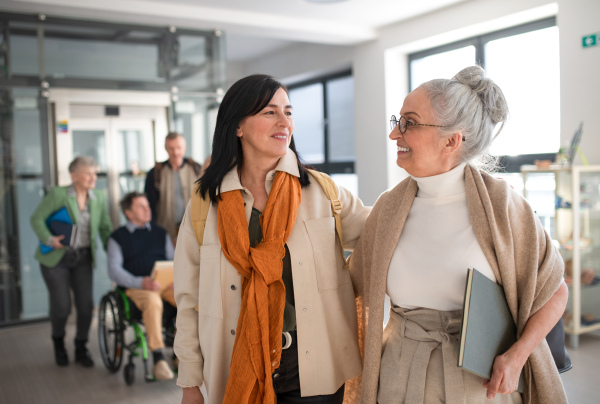 A happy mature woman student with book discussing with teacher in corridor in university.