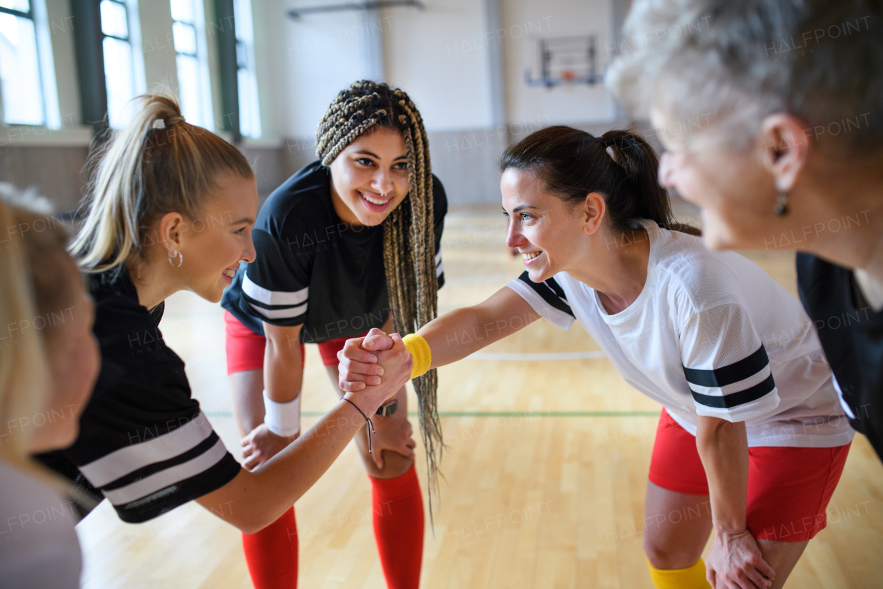 A group of young and old women in gym stacking hands together, sport team players.