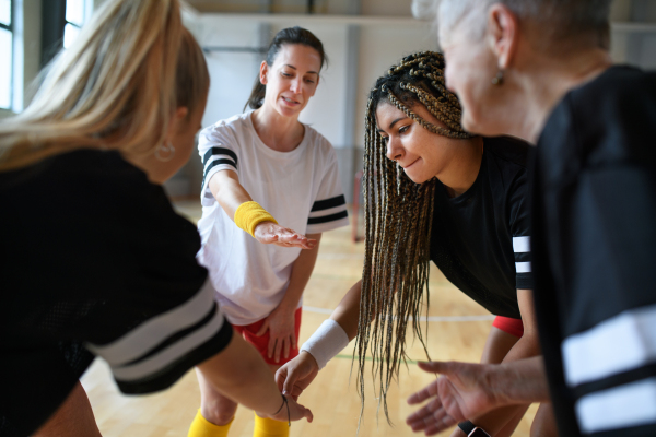 A group of young and old women in gym stacking hands together, sport team players.