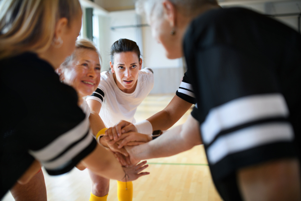 A group of multigenerational women in gym stacking hands together, sport team players.