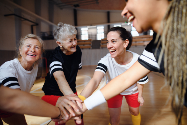 A group of multigenerational women in gym stacking hands together, sport team players.