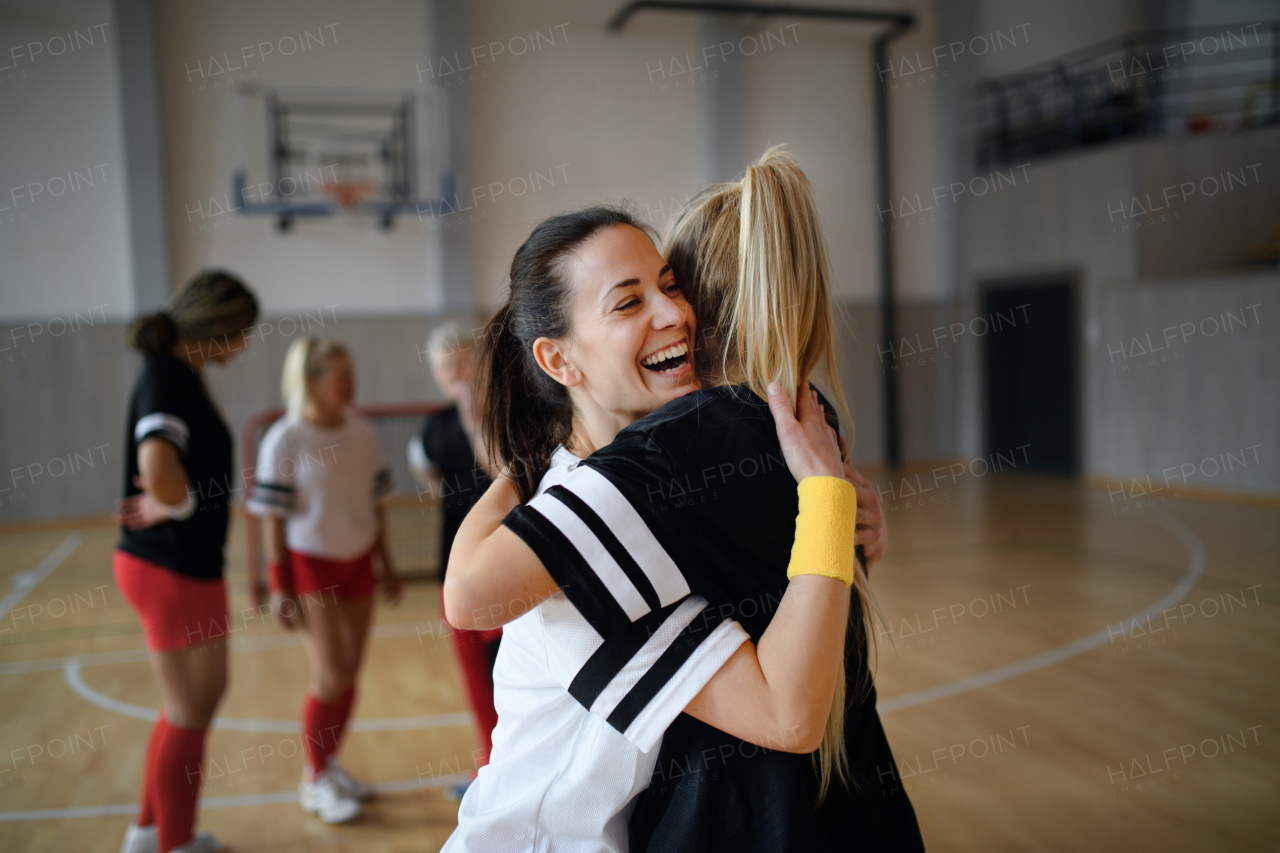 A group of young and old women, sports team players, in gym celebrating victory, hugging.