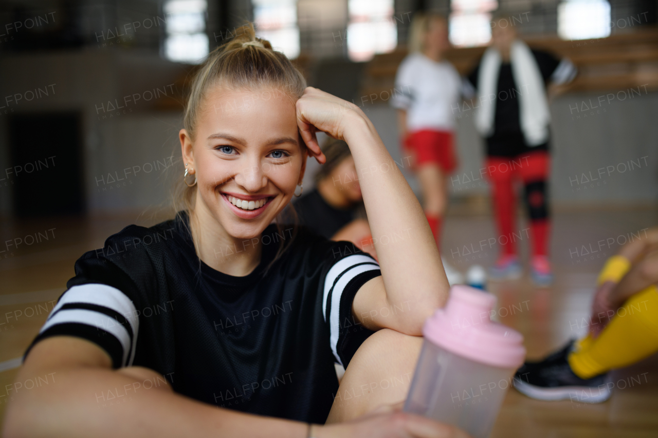 Portrait of young pretty woman, sports team players in gym sitting and resting after match with her teammates.