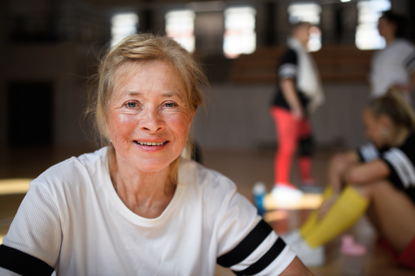 Happy senior woman stretching before basketball match in a gym.