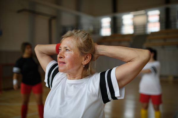 Senior woman stretching before basketball match in a gym.