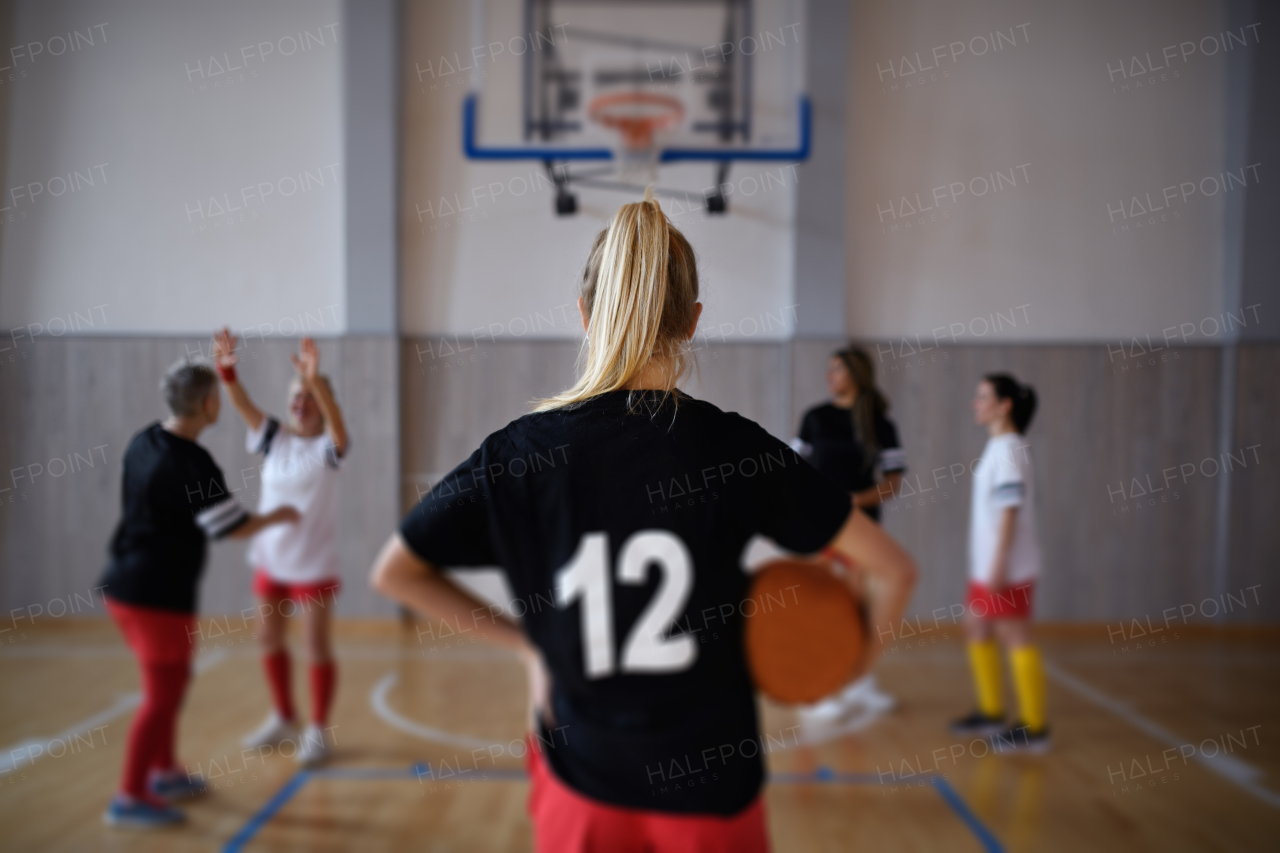 Rear view of young woman basketball player in gym during match.