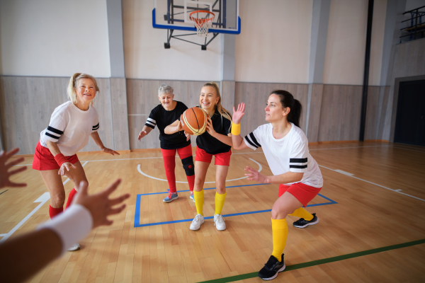 Multigenerational women playing a basketball match in gym.