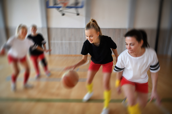 Young and senior women playing a basketball match in gym.