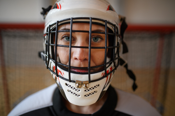 A close-up of woman floorball goalkeeper in helmet concetrating on game in gym.