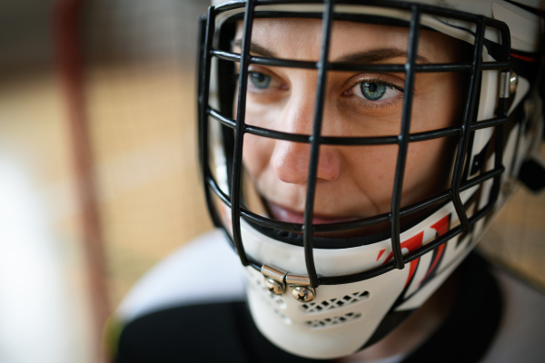 A close-up of woman floorball goalkeeper in helmet concetrating on game in gym.