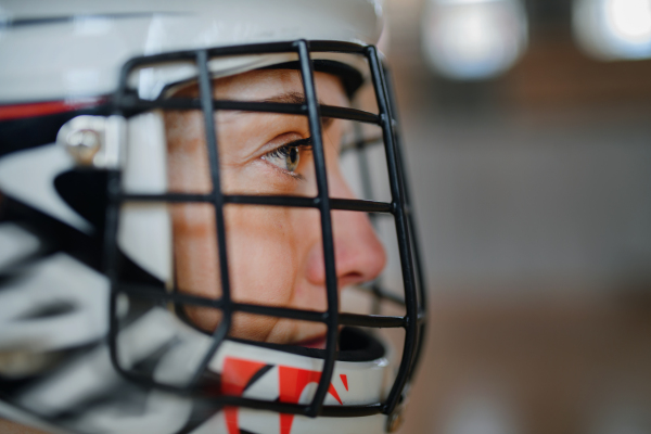 A close-up of woman floorball goalkeeper in helmet concetrating on game in gym.