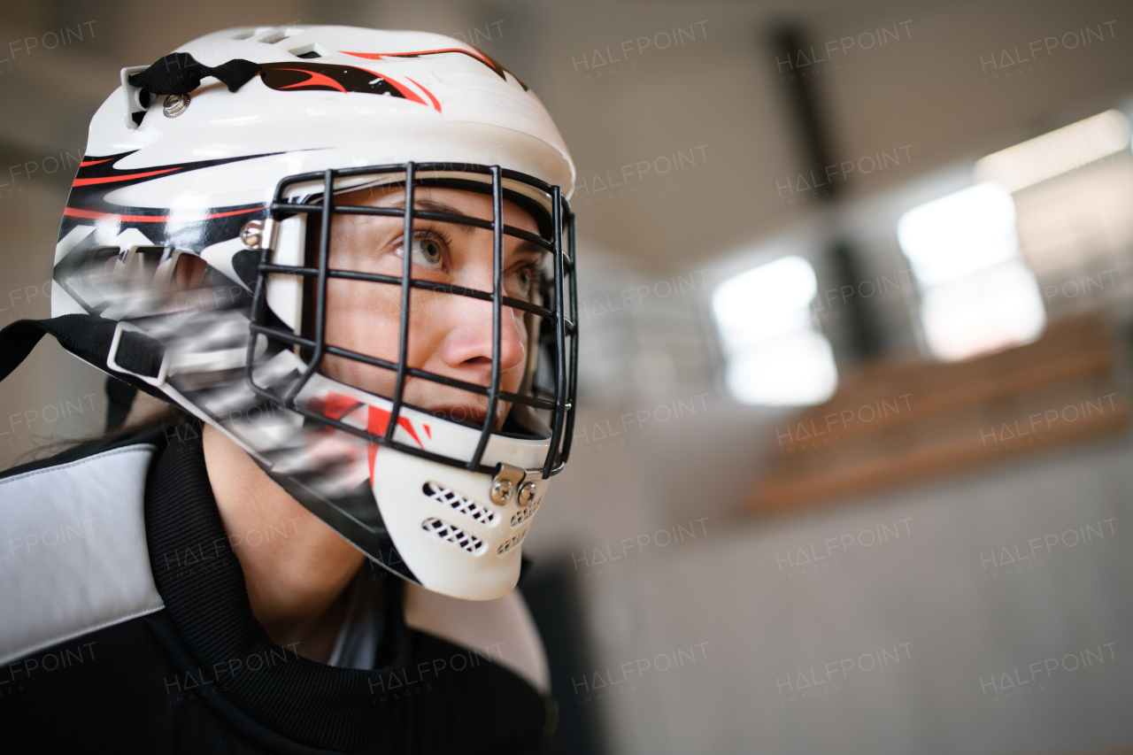 A close-up of woman floorball goalkeeper in helmet concetrating on game in gym.