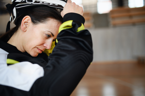 A close-up of woman floorball goalkeeper in helmet concetrating on game in gym.