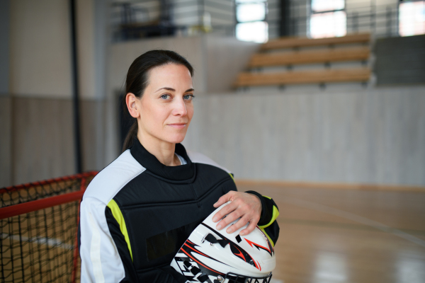 A close-up of woman floorball goalkeeper in helmet concetrating on game in gym.