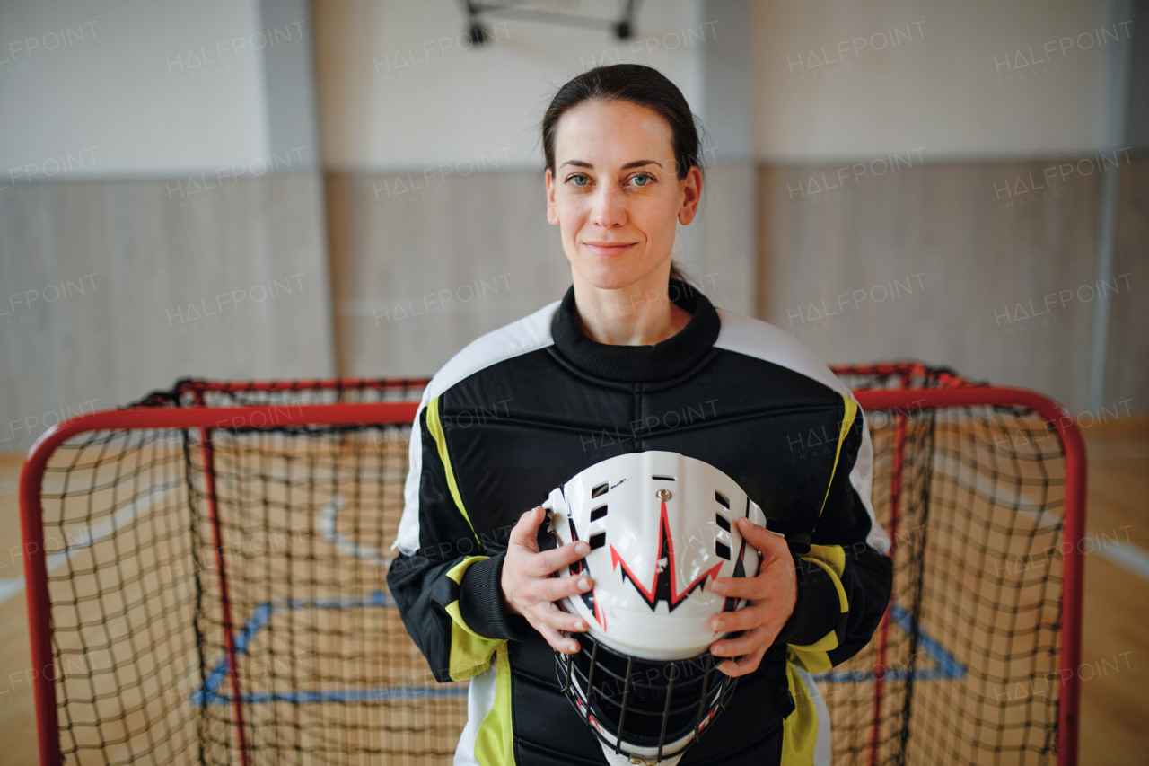 A close-up of woman floorball goalkeeper in helmet concetrating on game in gym.