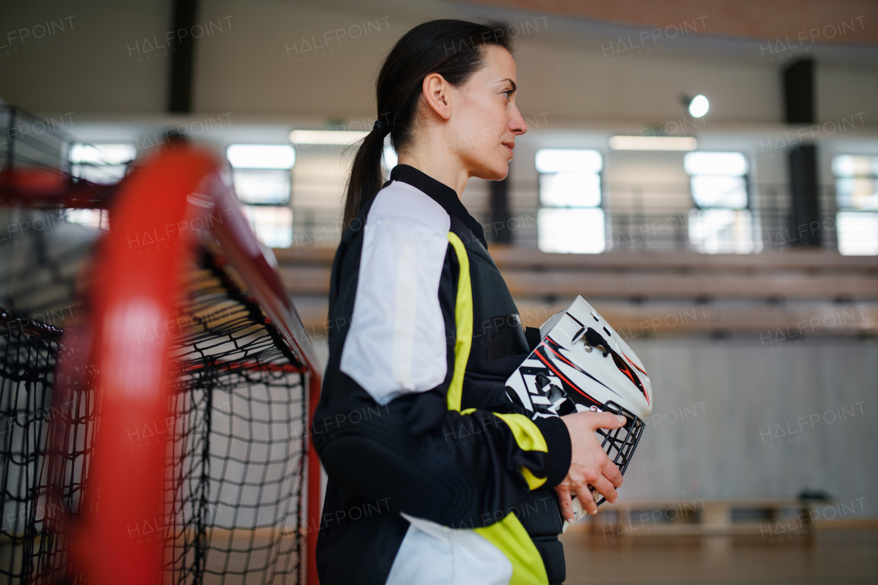 A close-up of woman floorball goalkeeper in helmet concetrating on game in gym.