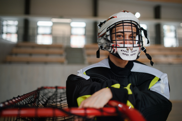 A close-up of woman floorball goalkeeper in helmet concetrating on game in gym.