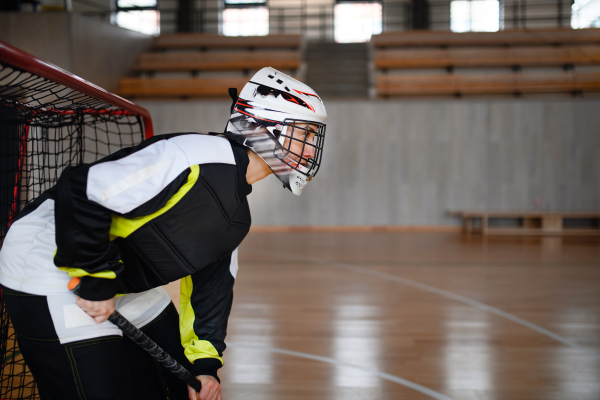 A close-up of woman floorball goalkeeper in helmet concetrating on game in gym.