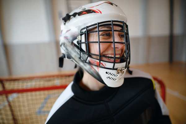 A close-up of woman floorball goalkeeper in helmet concetrating on game in gym.