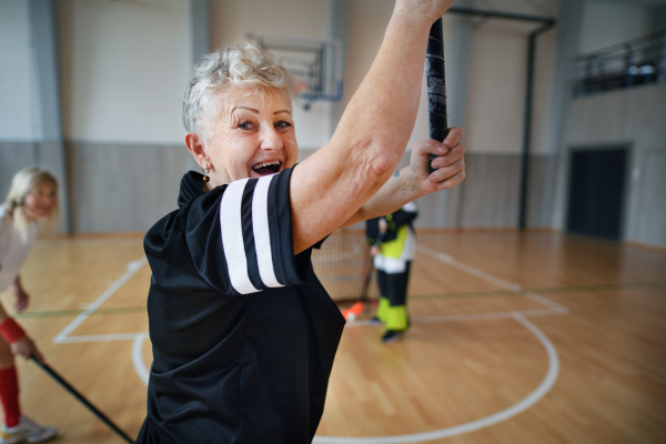 Excited senior woman playing floorball in gym with friends.