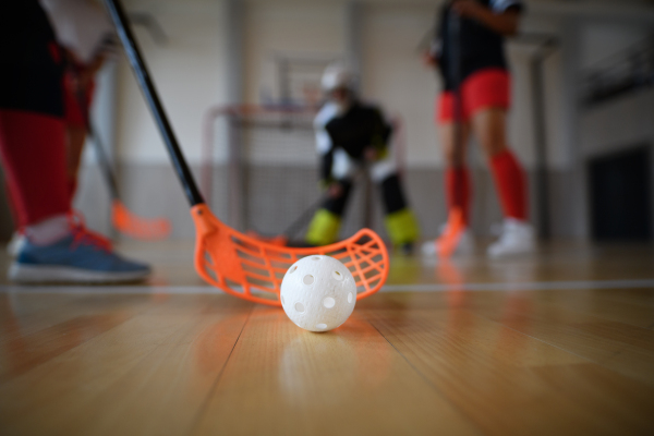 Close-up of floorball stick and ball during woman floorball match in a gym.