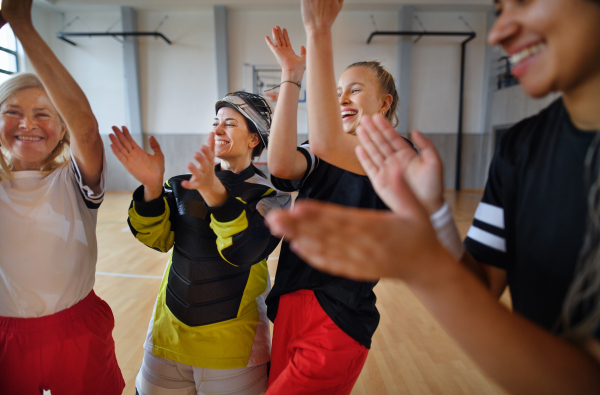 A group of young and old cheerful women, floorball team players, in gym cebrating victory.