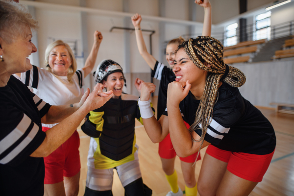 A group of young and old cheerful women, floorball team players, in gym cebrating victory.