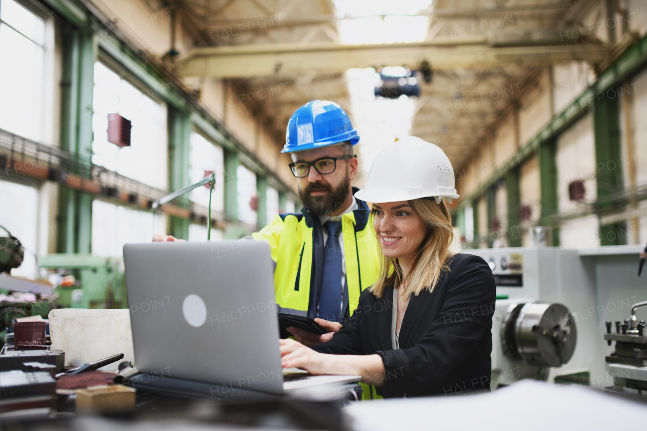 A male and female industrial engineers discussing factory's new machinery project and using laptop.