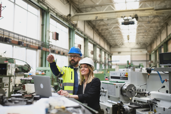 A male and female industrial engineers discussing factory's new machinery project and using laptop.