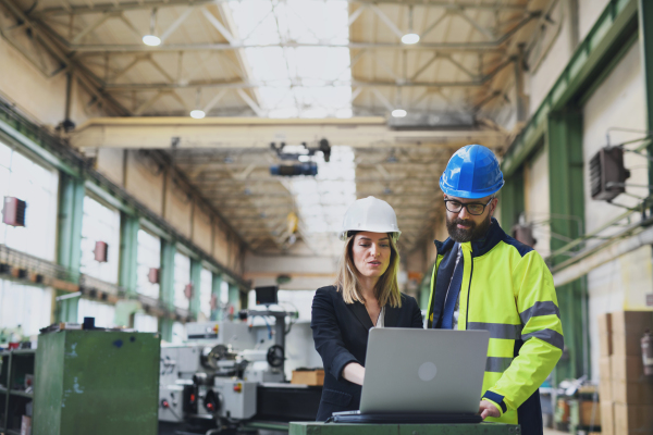 A male and female industrial engineers discussing factory's new machinery project and using laptop.