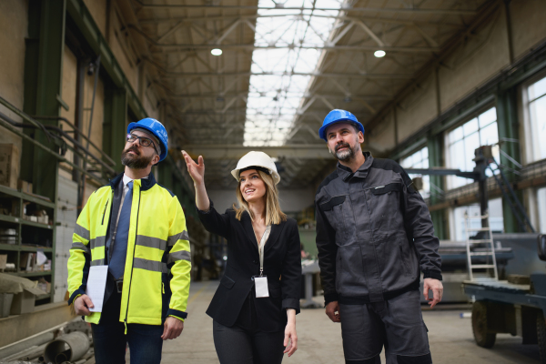 Manager supervisors and industrial worker in a uniform walking in large metal factory hall and talking.