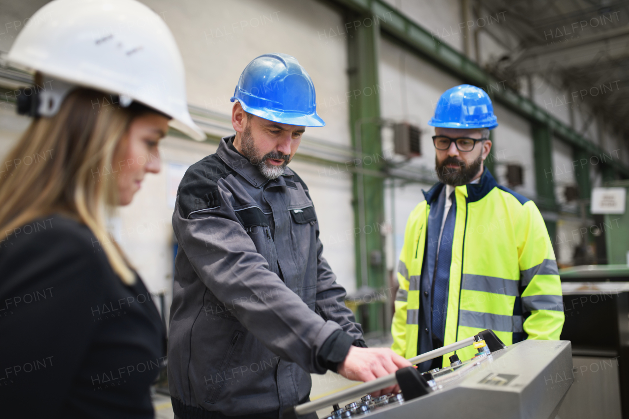 Manager supervisors and a industrial worker in uniform doing control in large metal factory hall and talking.