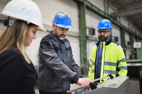 Manager supervisors and a industrial worker in uniform doing control in large metal factory hall and talking.