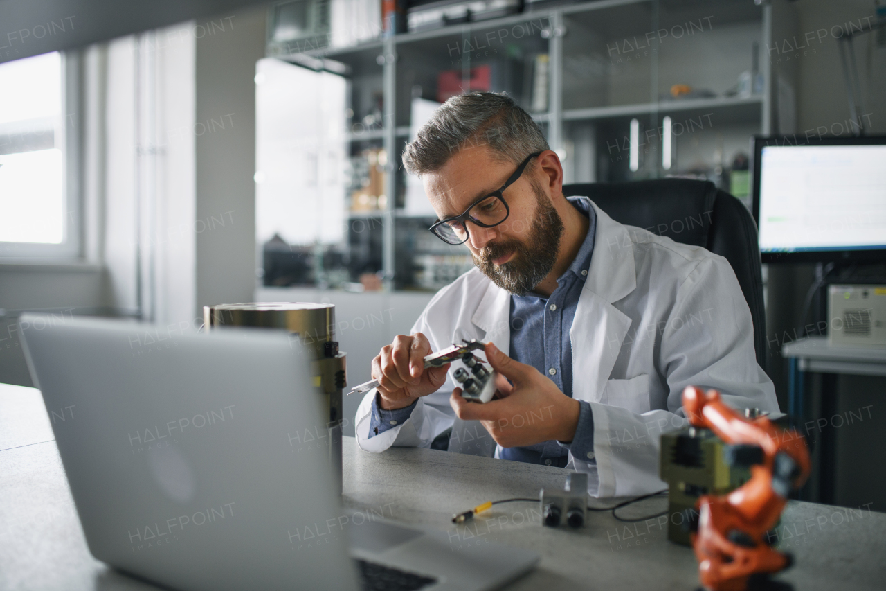 A robotics engineer working on desing of modern robotic arm adn sitting at dest in laboratory.