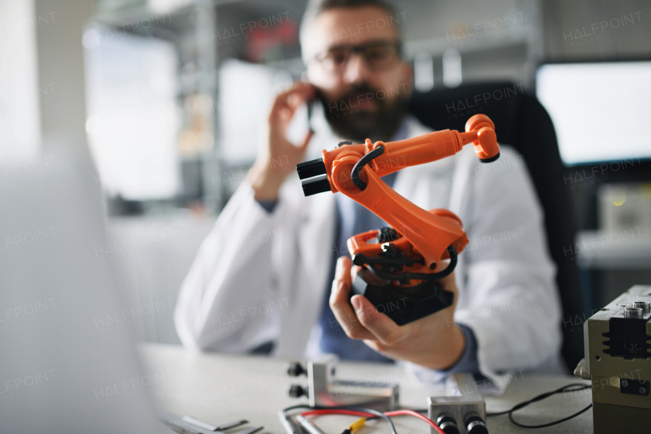 A robot arm industrial miniature figure in hand of robotics engineer working on laptop in laboratory.