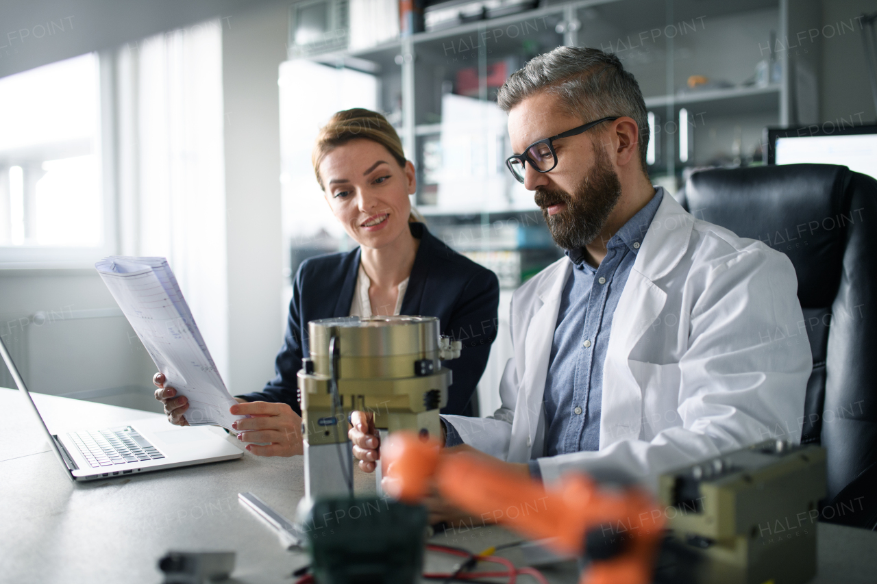 Robotics engineers working on a laptop and desinging modern robotic arm in laboratory.